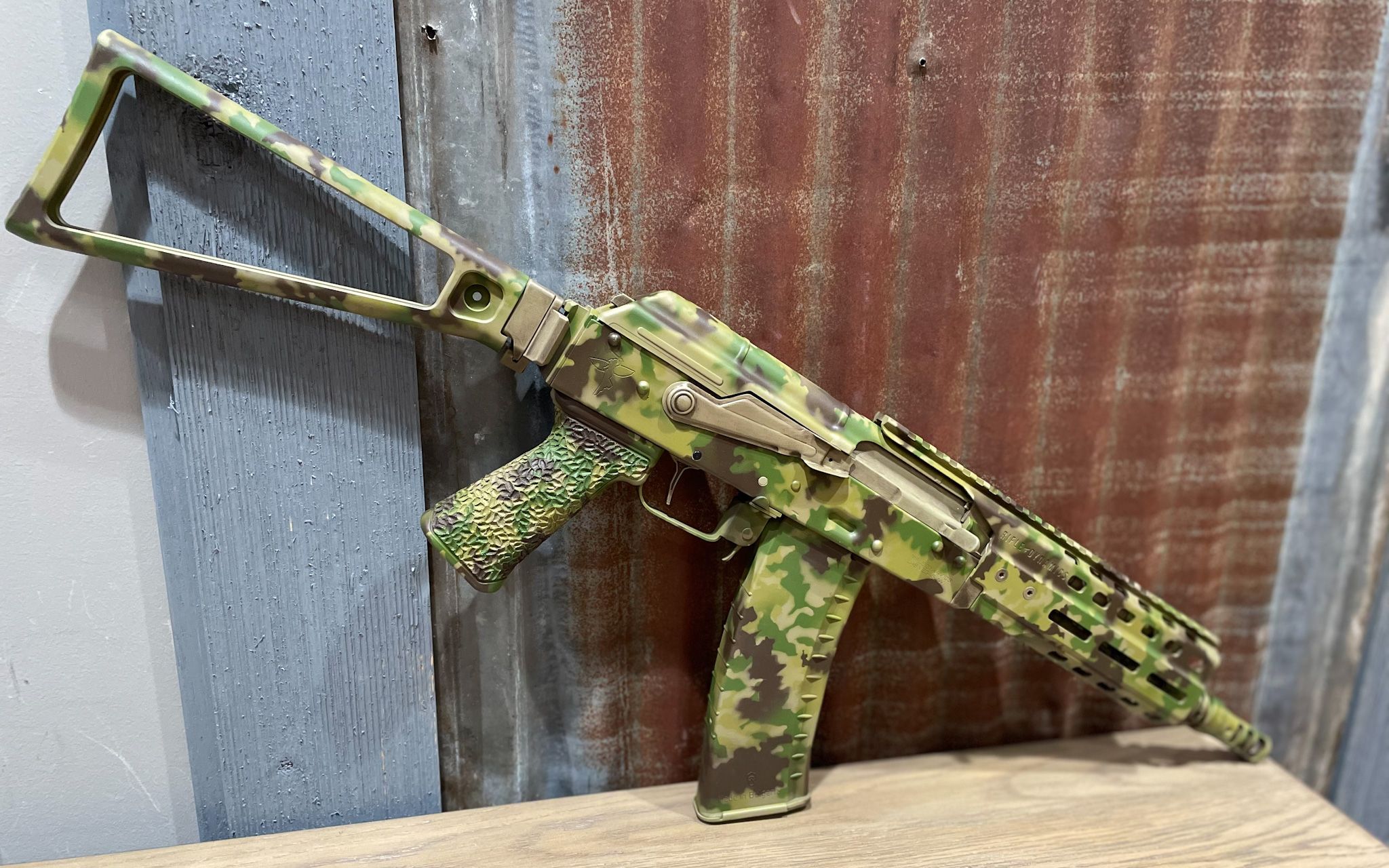 Custom Cerakote AK-style firearm with green woodland camouflage finish, showcasing precision coating and textured grip detail.
