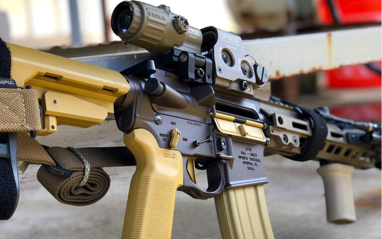 Two-tone Cerakote AR-15 rifle with tan and bronze finish, equipped with mounted optic and tactical accessories. ￼