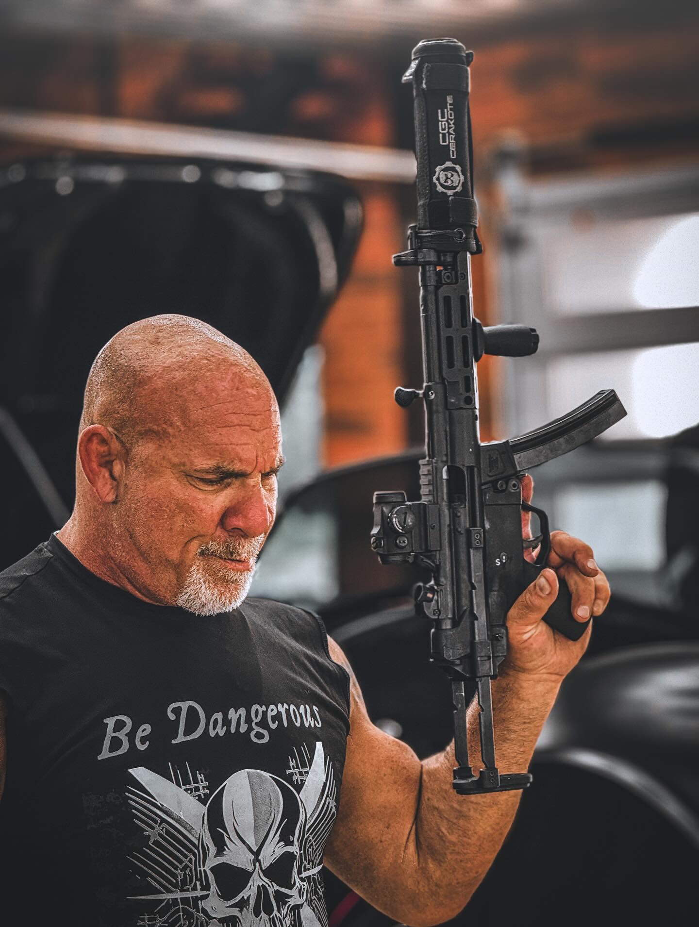 WWE Hall of Famer Bill Goldberg holding a custom Cerakote-finished firearm in a professional workshop setting.